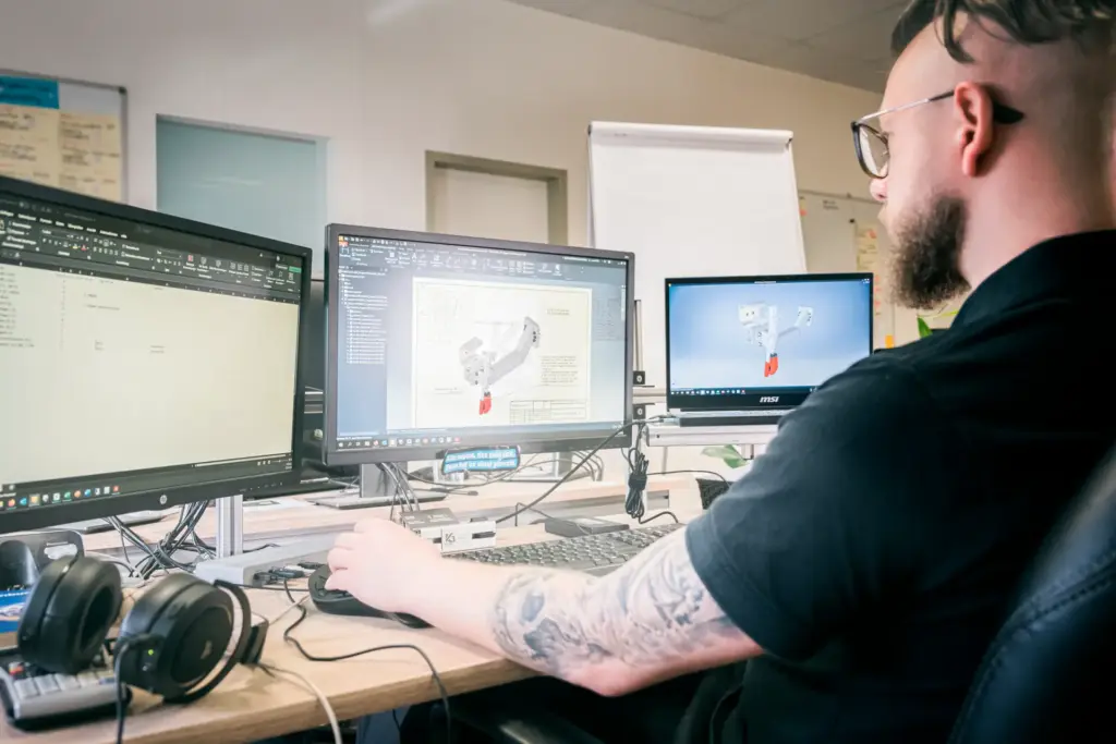 Seitliche Ansicht einer Person, die an einem Schreibtisch sitzt und Animationen erstellt. Die Person verwendet dabei drei Bildschirme
